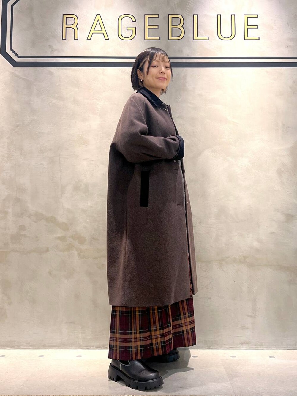 ブラウン系のステンカラーコート、レッド系のスカート、ブラック系のブーツを着用したレディースの秋コーディネートの6枚目の写真