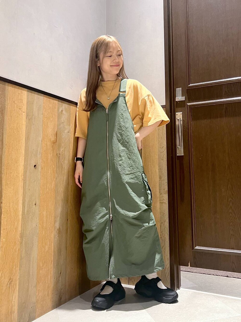 グリーン系のジャンパースカート、ブラック系のスニーカー、イエロー系のTシャツ/カットソーを着用したレディースの夏コーディネートの2枚目の写真