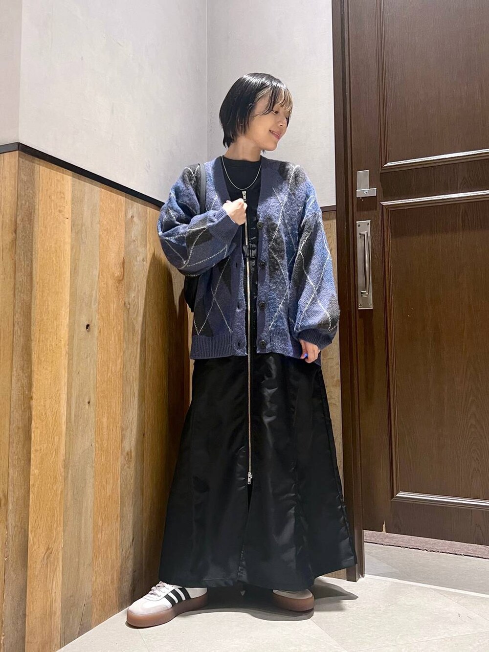 ブラック系のショルダーバッグ、ブルー系のカーディガン/ボレロ、ブラック系のジャンパースカートを着用したレディースの秋コーディネートの2枚目の写真