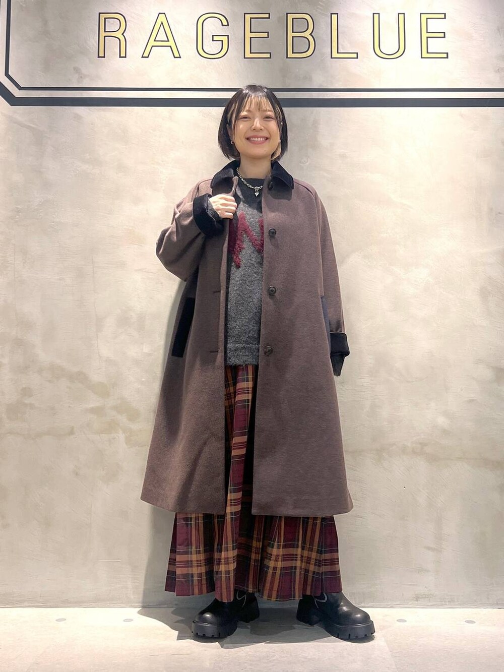 ブラウン系のステンカラーコート、レッド系のスカート、ブラック系のブーツを着用したレディースの秋コーディネートの4枚目の写真