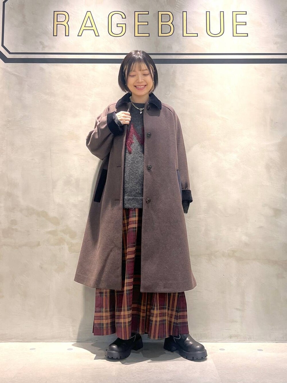 ブラウン系のステンカラーコート、レッド系のスカート、ブラック系のブーツを着用したレディースの秋コーディネートの5枚目の写真