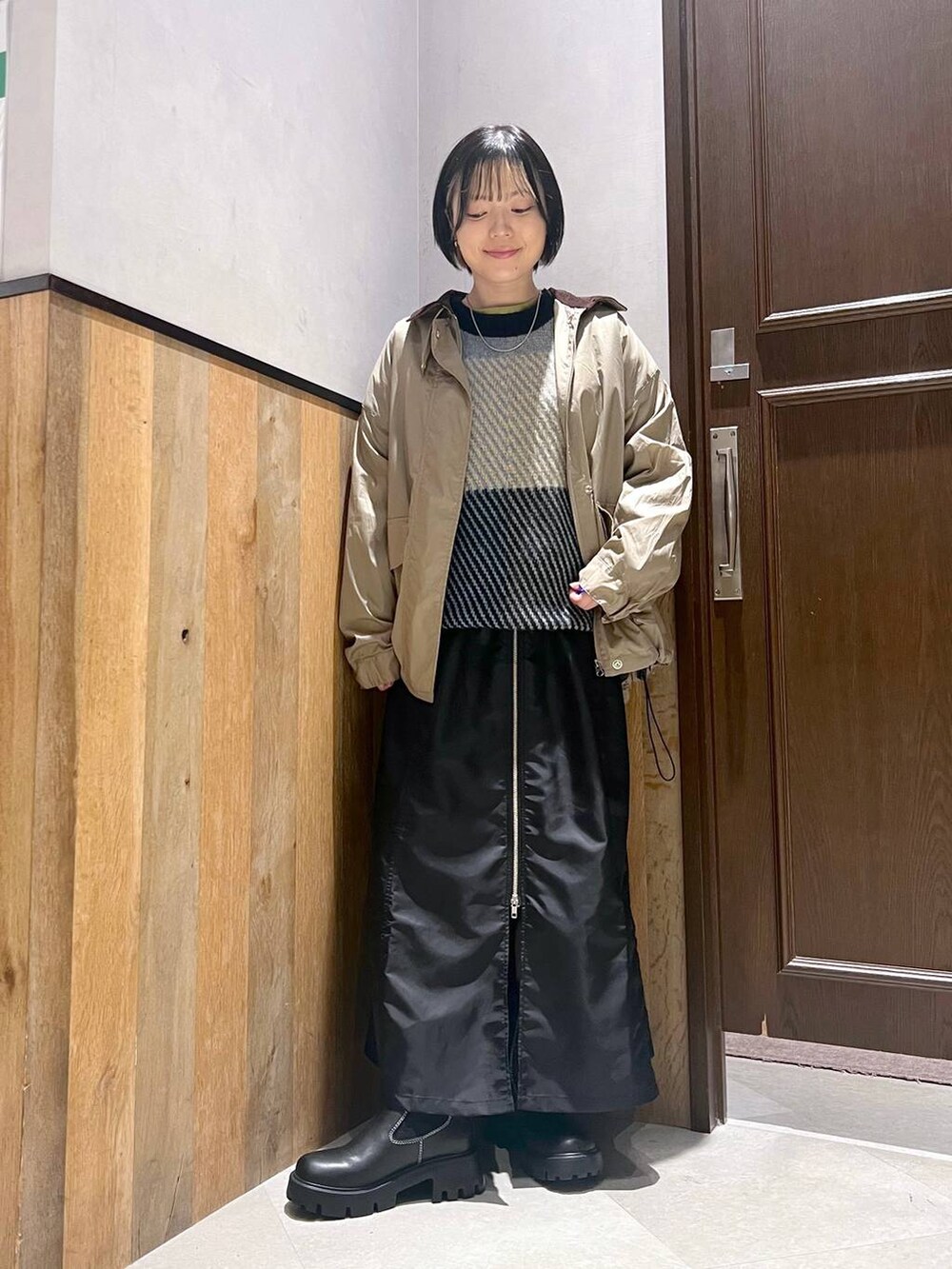 ブラック系のブーツ、ベージュ系のミリタリージャケット、ブラック系のジャンパースカートを着用したレディースの秋コーディネートの2枚目の写真