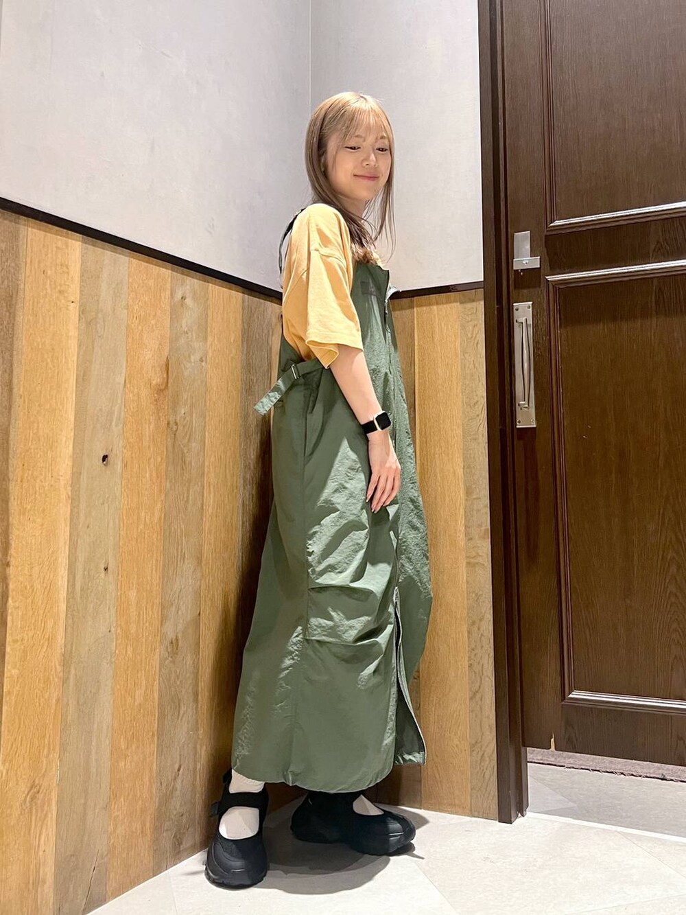グリーン系のジャンパースカート、ブラック系のスニーカー、イエロー系のTシャツ/カットソーを着用したレディースの夏コーディネートの3枚目の写真