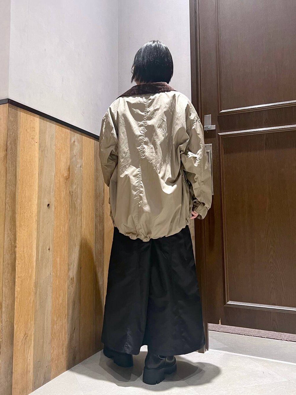 ブラック系のブーツ、ベージュ系のミリタリージャケット、ブラック系のジャンパースカートを着用したレディースの秋コーディネートの4枚目の写真