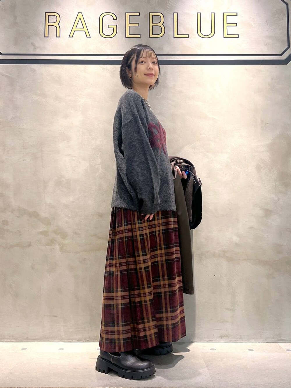ブラウン系のステンカラーコート、レッド系のスカート、ブラック系のブーツを着用したレディースの秋コーディネートの2枚目の写真