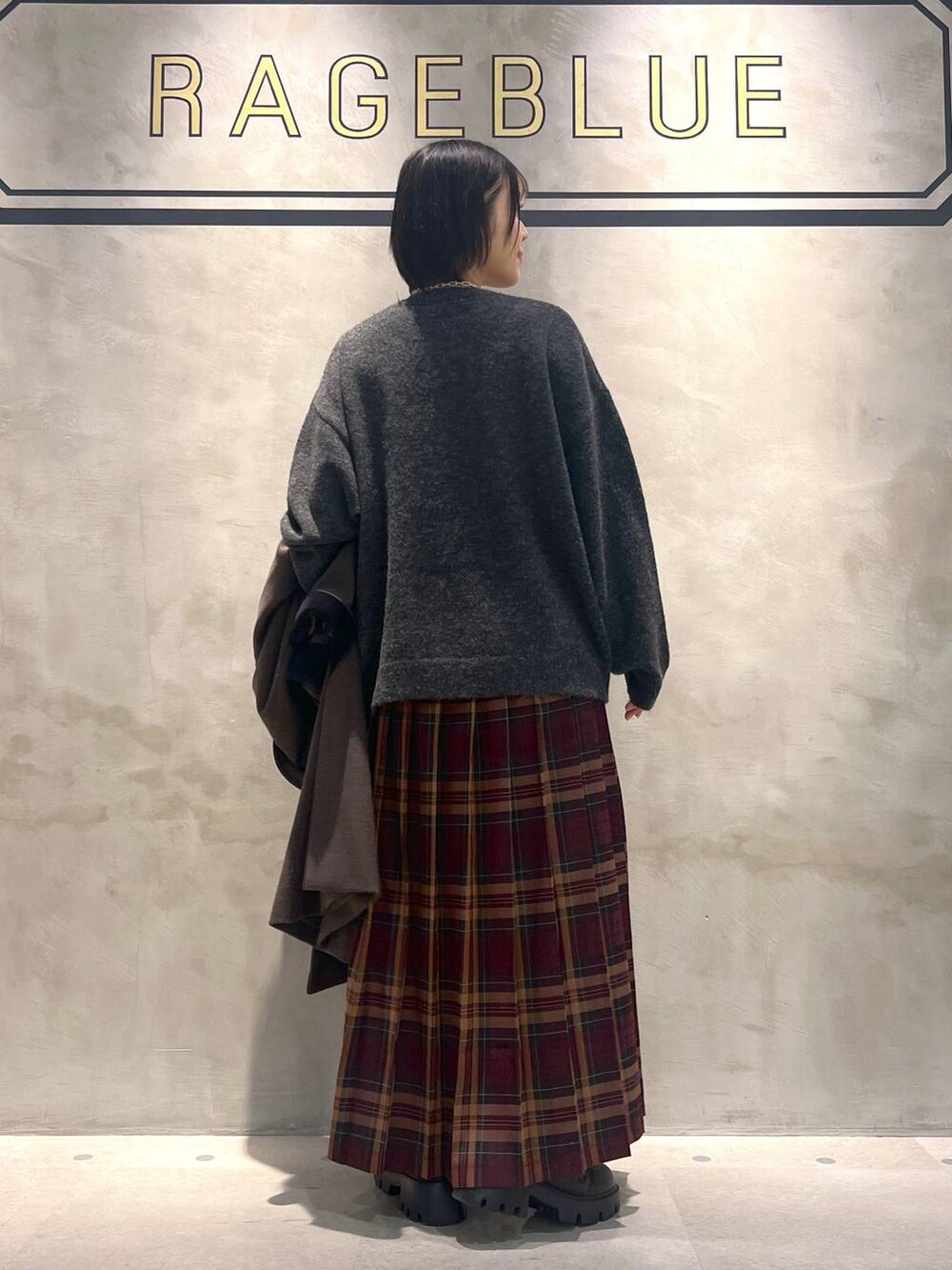 ブラウン系のステンカラーコート、レッド系のスカート、ブラック系のブーツを着用したレディースの秋コーディネートの3枚目の写真