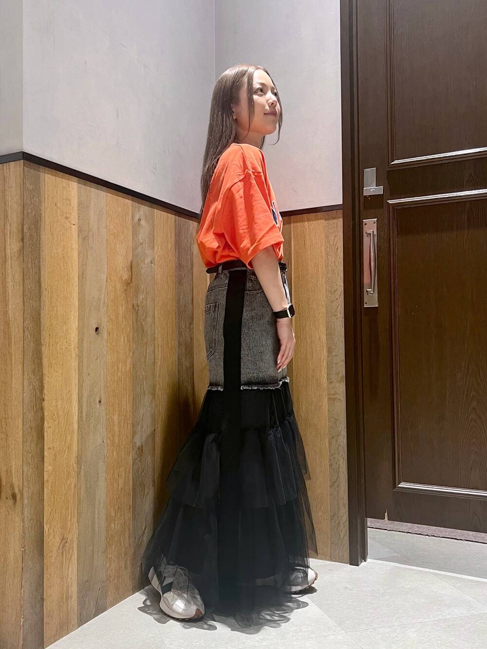 オレンジ系のTシャツ/カットソー、ホワイト系のスニーカー、ブラック系のデニムスカートを着用したレディースの夏コーディネートの2枚目の写真