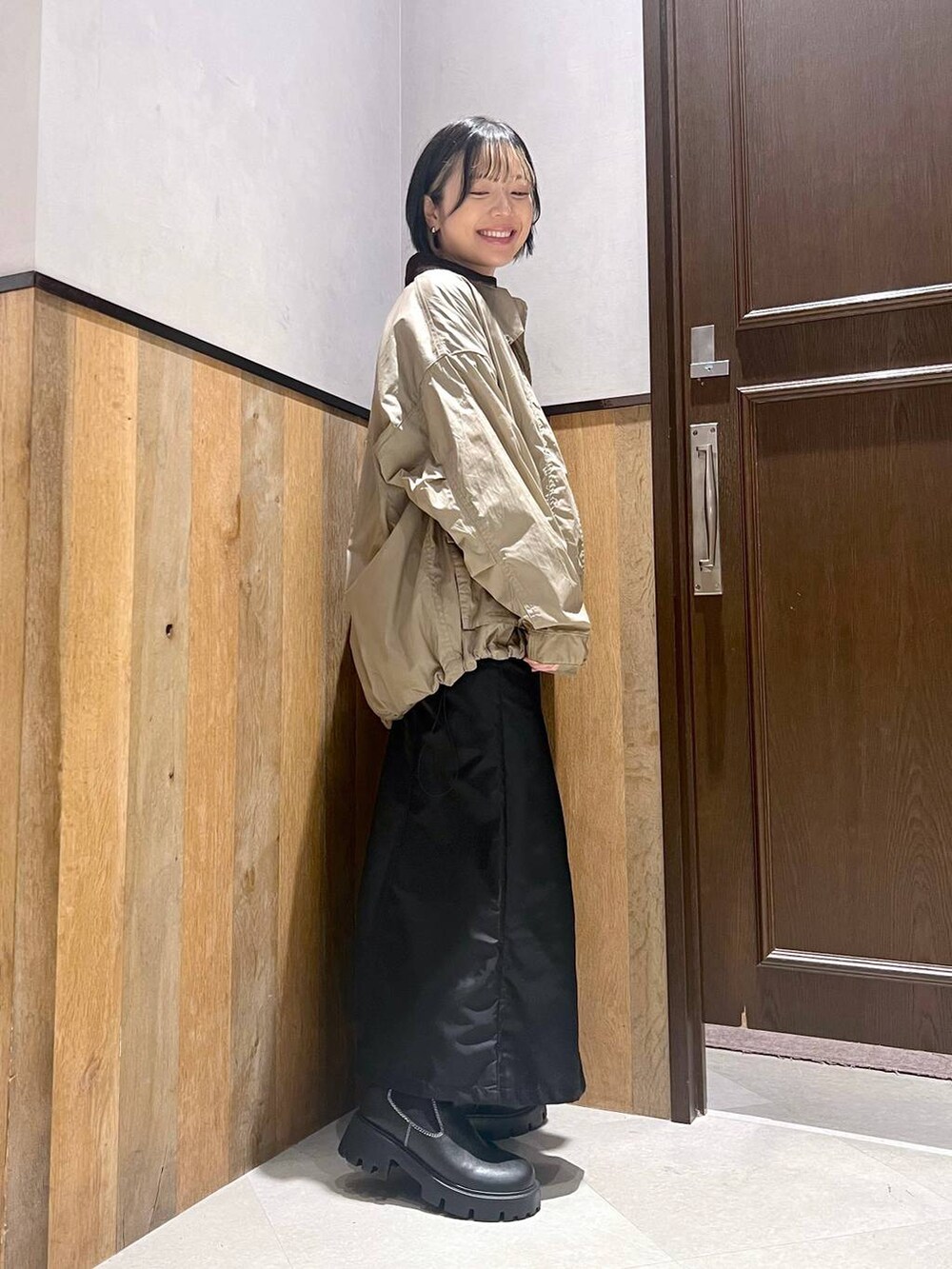 ブラック系のブーツ、ベージュ系のミリタリージャケット、ブラック系のジャンパースカートを着用したレディースの秋コーディネートの3枚目の写真