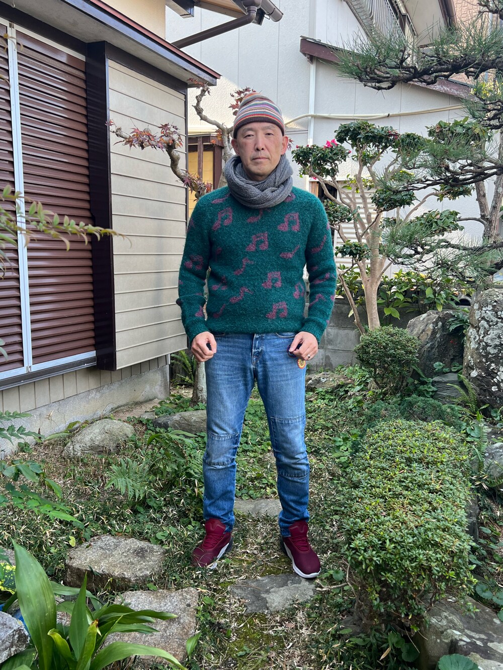 グリーン系のニット/セーター、ブルー系のデニムパンツ、レッド系のスニーカーを着用したメンズの冬コーディネートの2枚目の写真