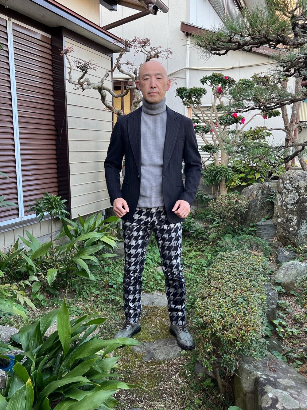 グレー系のニット/セーター、ブラック系のテーラードジャケット、ホワイト系のパンツを着用したメンズの冬コーディネートの2枚目の写真