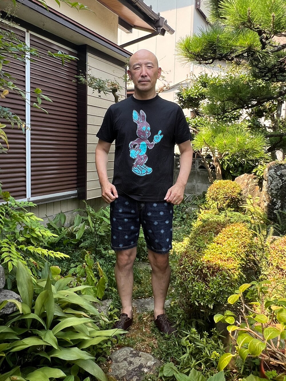 ブラック系のTシャツ/カットソー、ブルー系のデニムパンツ、ブラウン系のスニーカーを着用したメンズの夏コーディネートの2枚目の写真