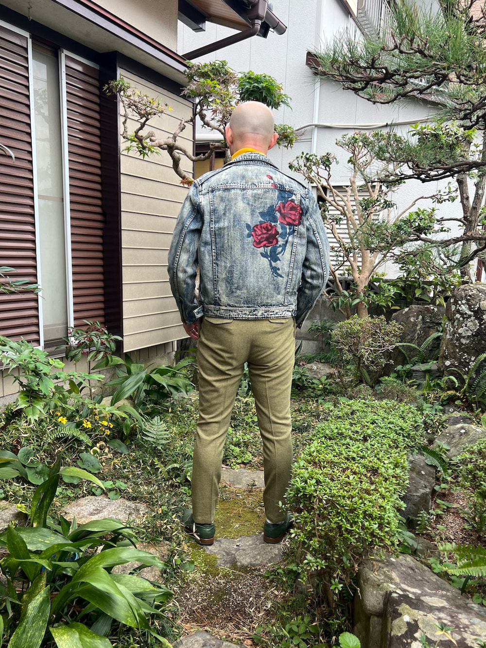 イエロー系のTシャツ/カットソー、ブルー系のライダースジャケット、グリーン系のスラックスを着用したメンズの冬コーディネートの2枚目の写真