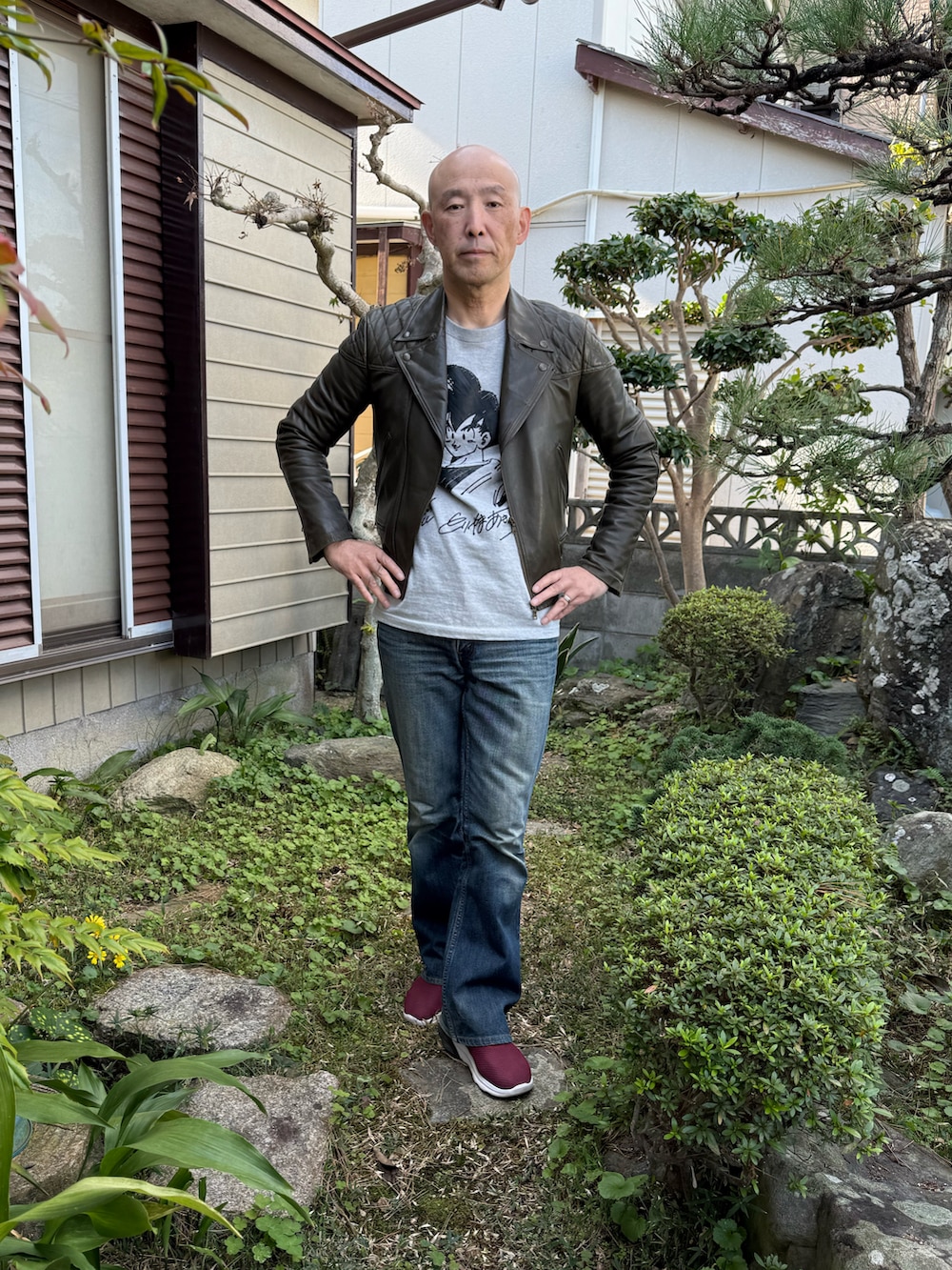 グレー系のTシャツ/カットソー、グリーン系のライダースジャケット、ブルー系のデニムパンツを着用したメンズの冬コーディネートの2枚目の写真