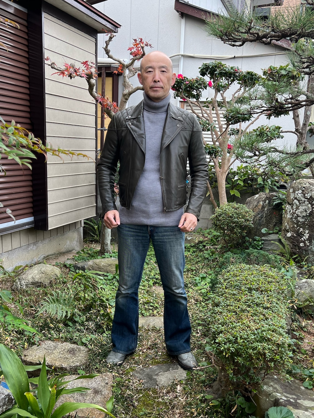 グリーン系のライダースジャケット、グレー系のニット/セーター、ブルー系のデニムパンツを着用したメンズの冬コーディネートの2枚目の写真