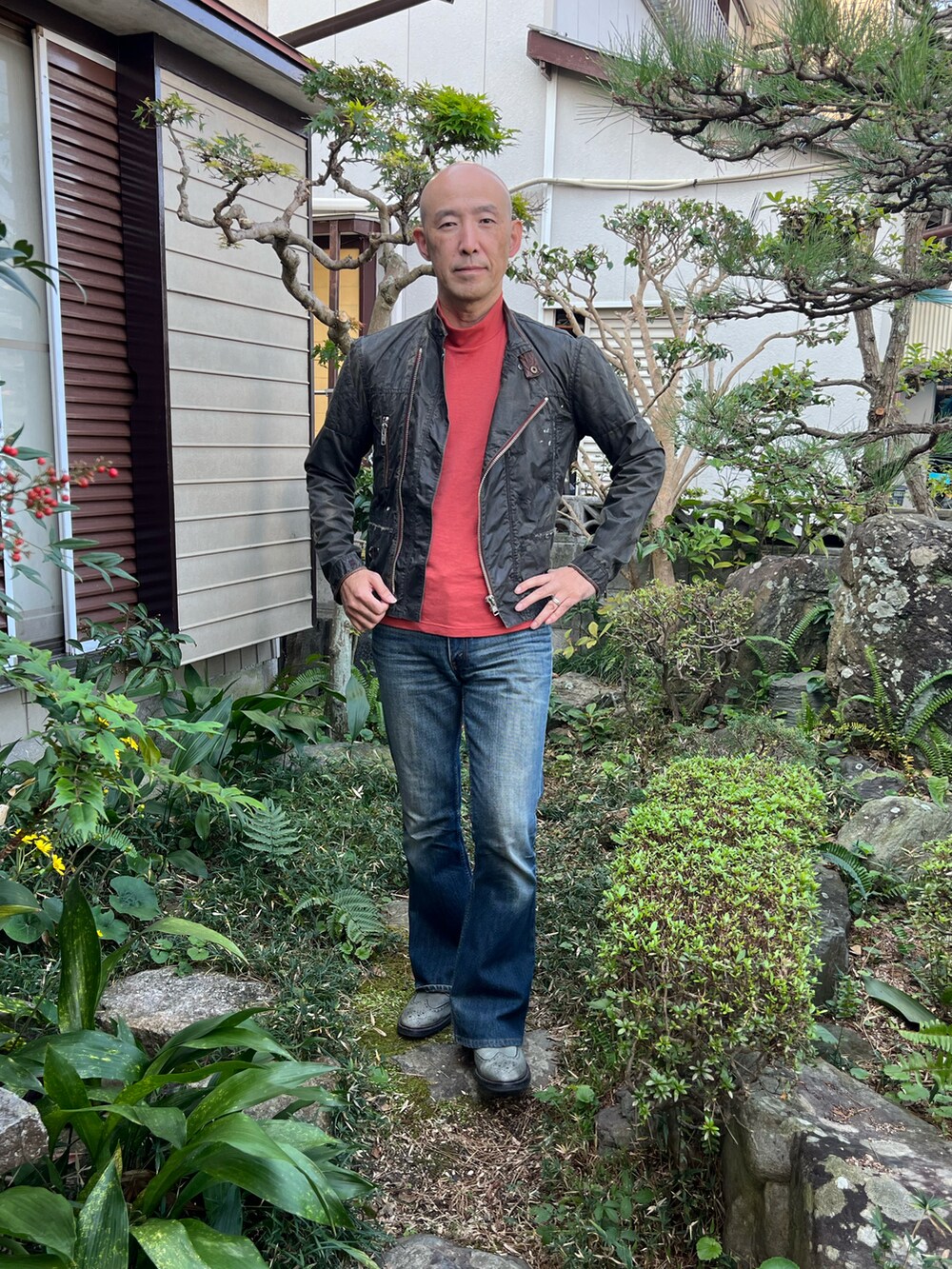 オレンジ系のTシャツ/カットソー、グレー系のライダースジャケット、ブルー系のデニムパンツを着用したメンズの秋コーディネートの2枚目の写真