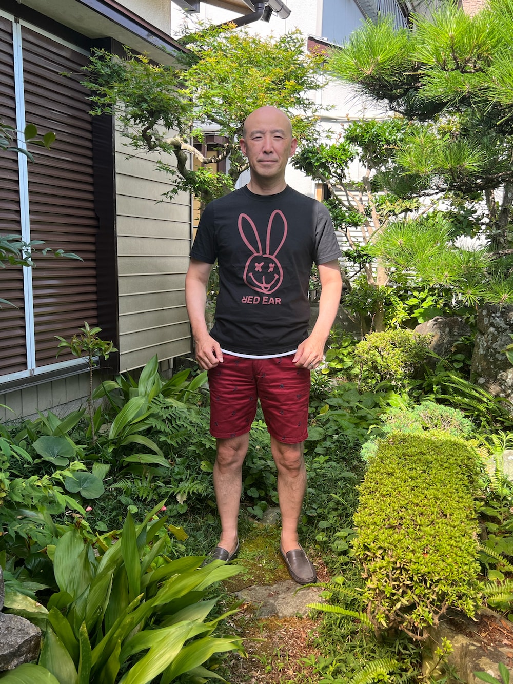 ブラック系のTシャツ/カットソー、レッド系のパンツ、ブルー系のローファーを着用したメンズの夏コーディネートの2枚目の写真