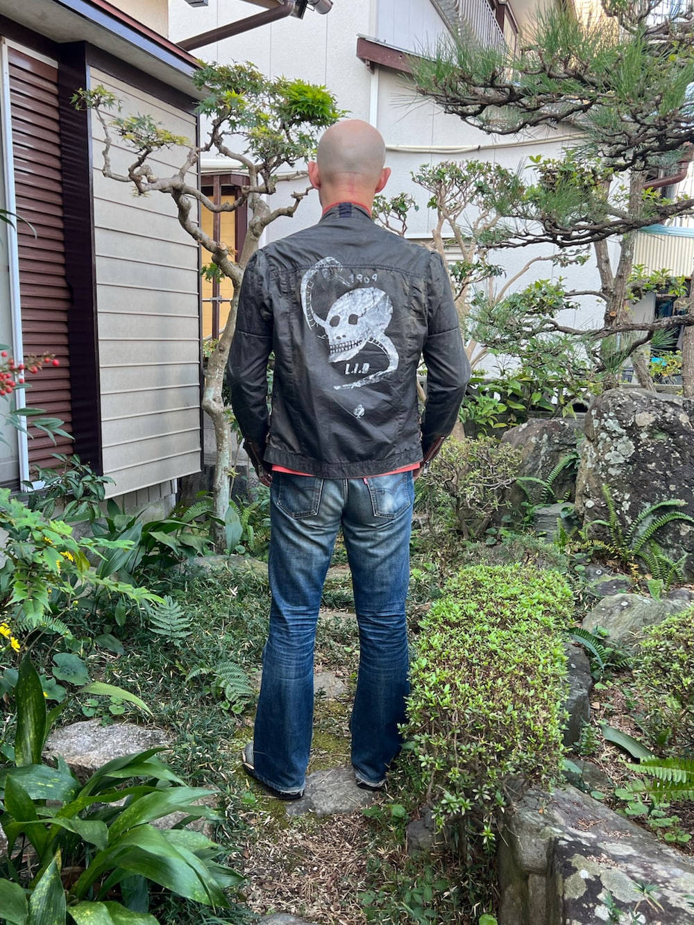 オレンジ系のTシャツ/カットソー、グレー系のライダースジャケット、ブルー系のデニムパンツを着用したメンズの秋コーディネートの3枚目の写真