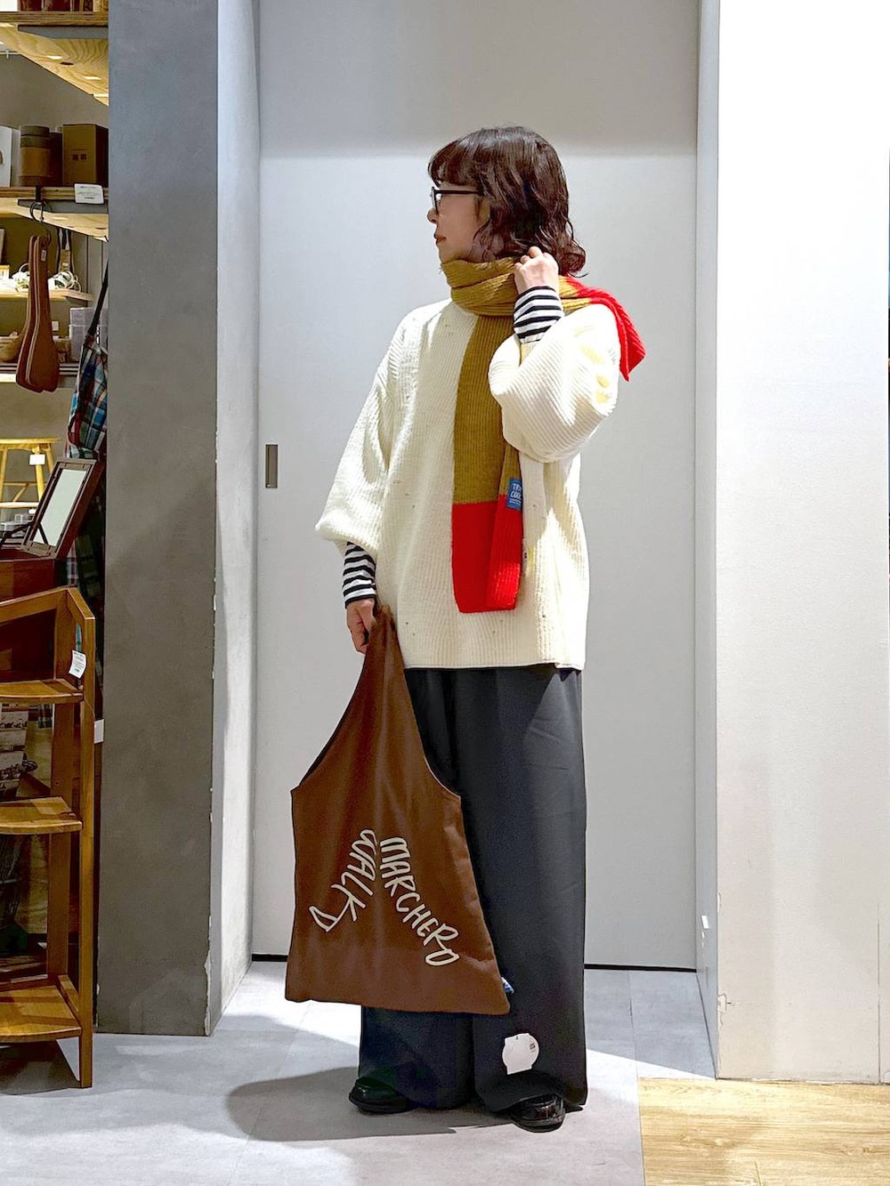 ホワイト系のニット/セーター、ブラウン系のエコバッグ/サブバッグ、グレー系のスラックスを着用したレディースの冬コーディネートの2枚目の写真