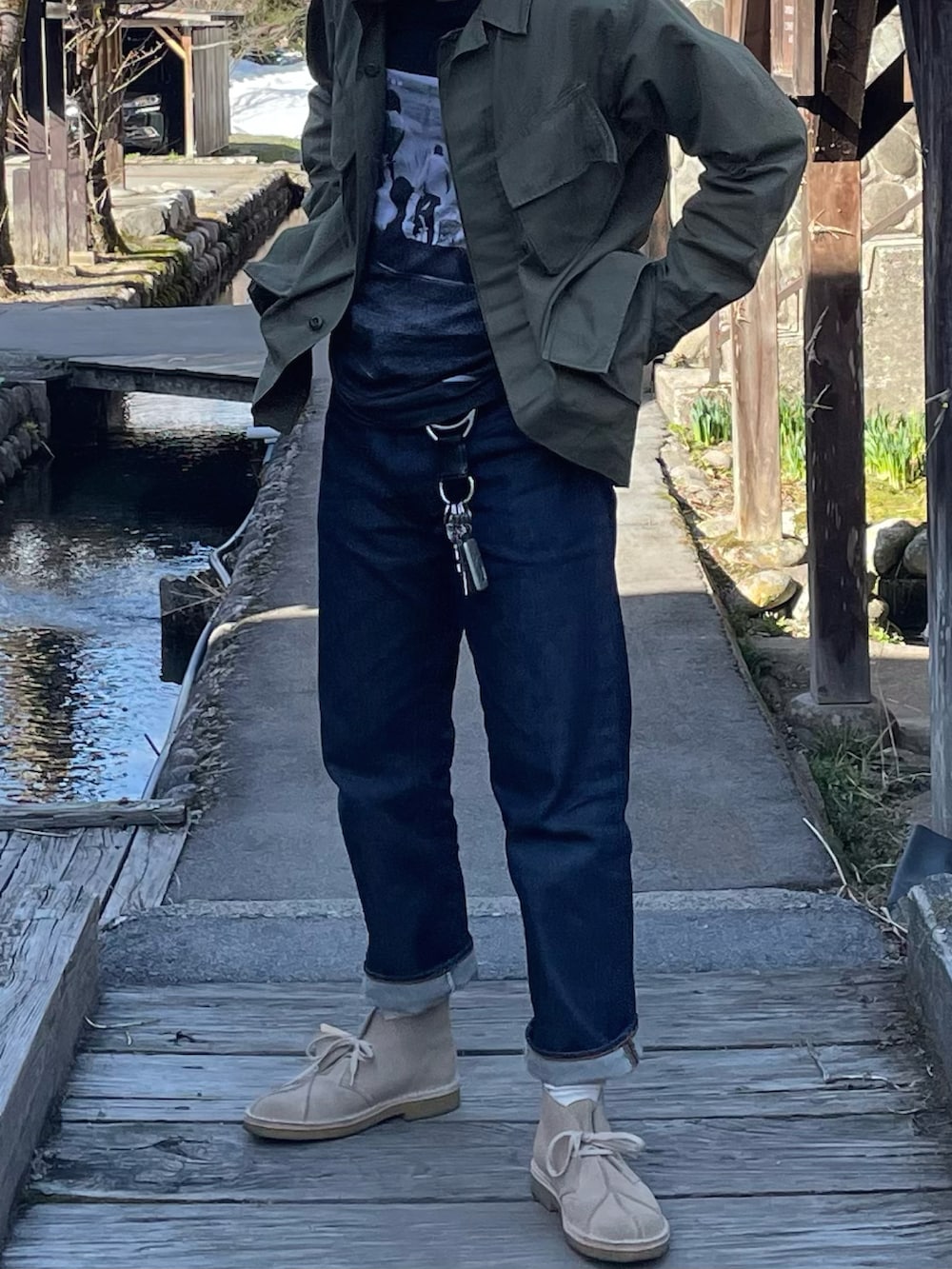 グリーン系のミリタリージャケット、ブラック系のTシャツ/カットソー、ブルー系のデニムパンツを着用したメンズの冬コーディネートの2枚目の写真