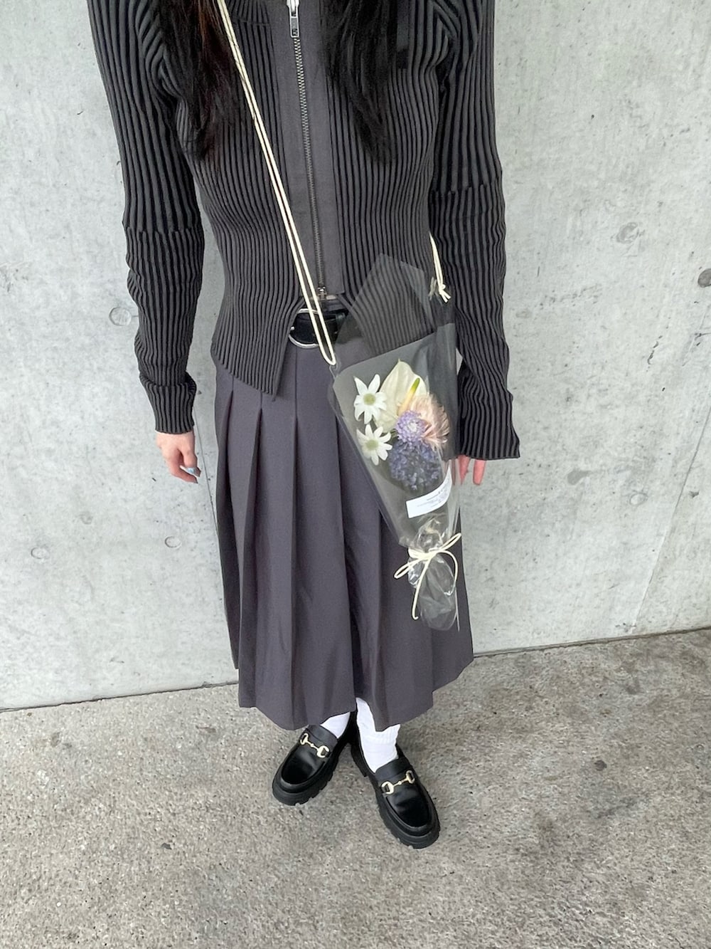 ブラック系のローファー、グレー系のスカート、ブラック系のニット/セーターを着用したレディースの春コーディネートの2枚目の写真