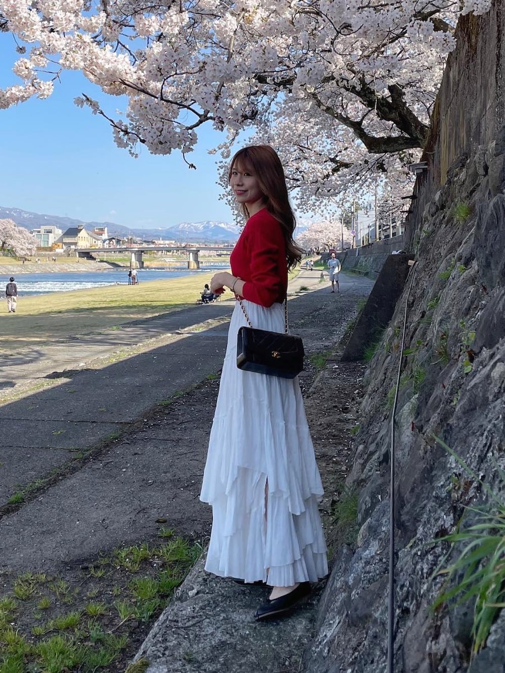 ホワイト系のスカート、ブラック系のバッグ、レッド系のニット/セーターを着用したレディースの春コーディネートの2枚目の写真