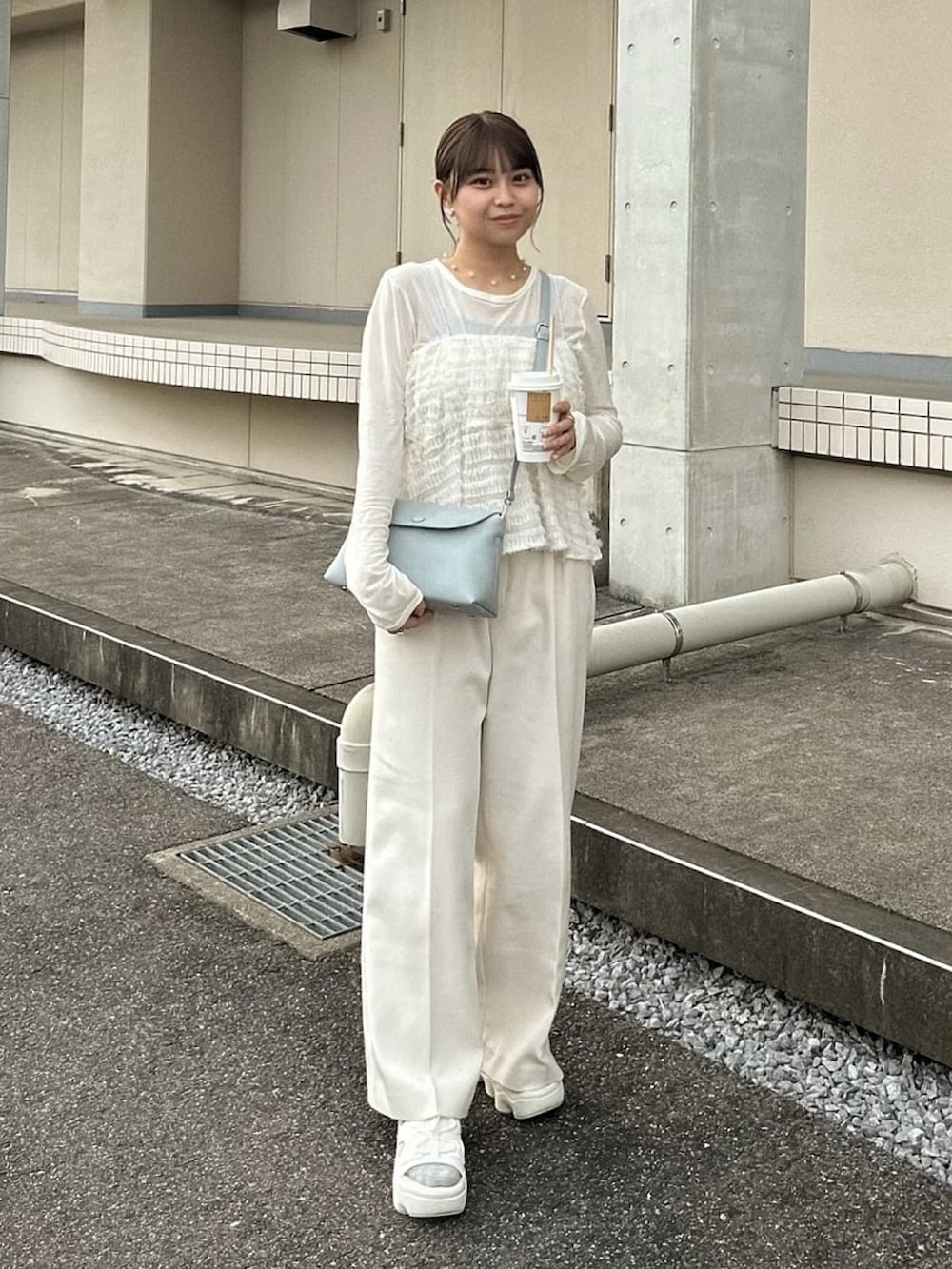 ホワイト系のスラックス、ホワイト系のキャミソール、ブルー系のショルダーバッグを着用したレディースの春コーディネートの2枚目の写真