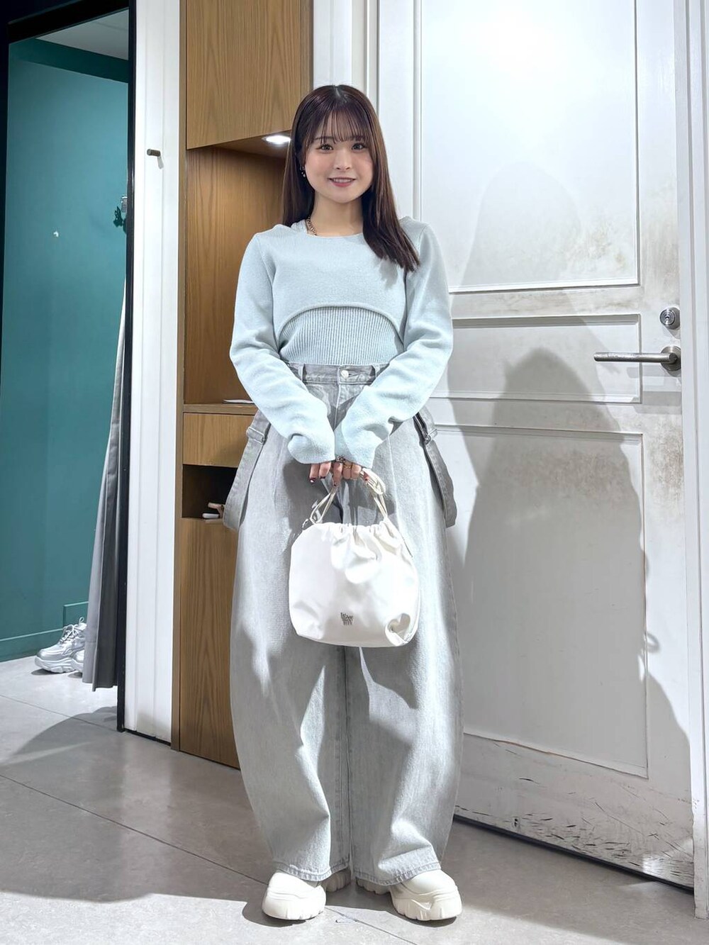 グレー系のデニムパンツ、ホワイト系のショルダーバッグ、グリーン系のニット/セーターを着用したレディースの春コーディネートの2枚目の写真