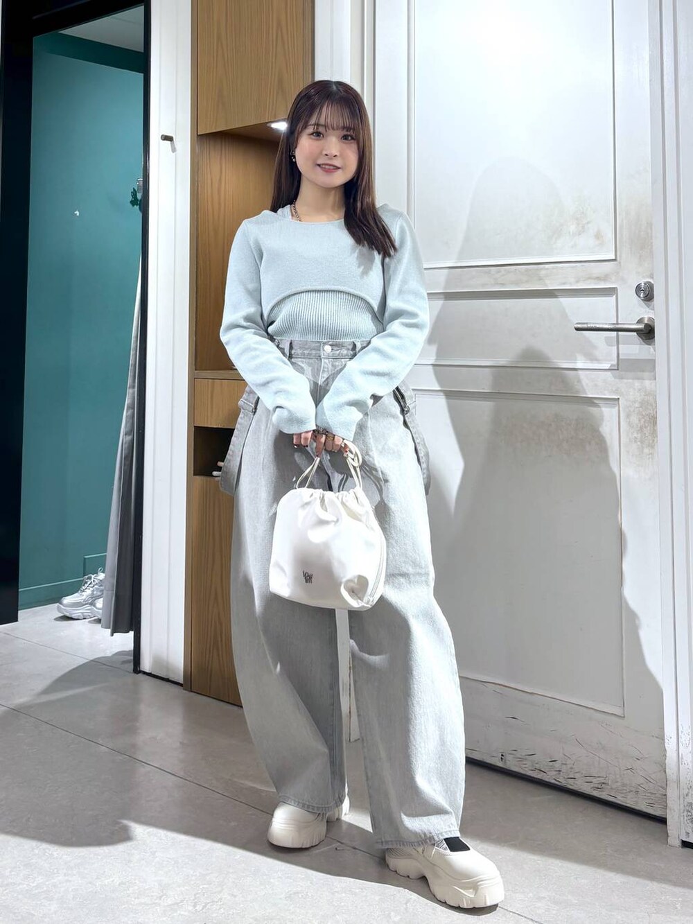 グレー系のデニムパンツ、ホワイト系のショルダーバッグ、グリーン系のニット/セーターを着用したレディースの春コーディネートの4枚目の写真