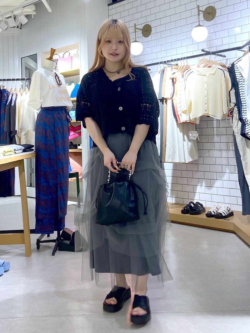 ブラック系のニット/セーター、グレー系のスカート、ブラック系のサンダルを着用したレディースの夏コーディネートの2枚目の写真