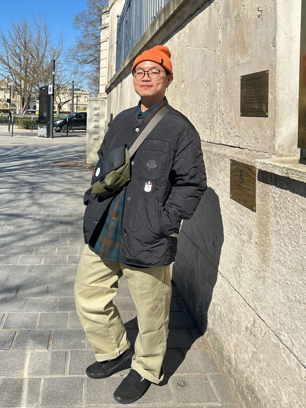 ブラック系のスニーカー、ベージュ系のパンツ、グリーン系のトップスを着用したメンズの春コーディネートの2枚目の写真