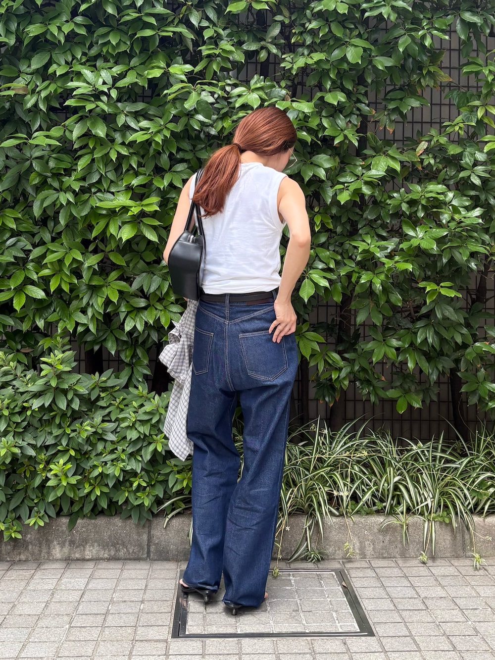 ブルー系のデニムパンツ、ブラック系のショルダーバッグ、ホワイト系のタンクトップを着用したレディースの夏コーディネートの4枚目の写真
