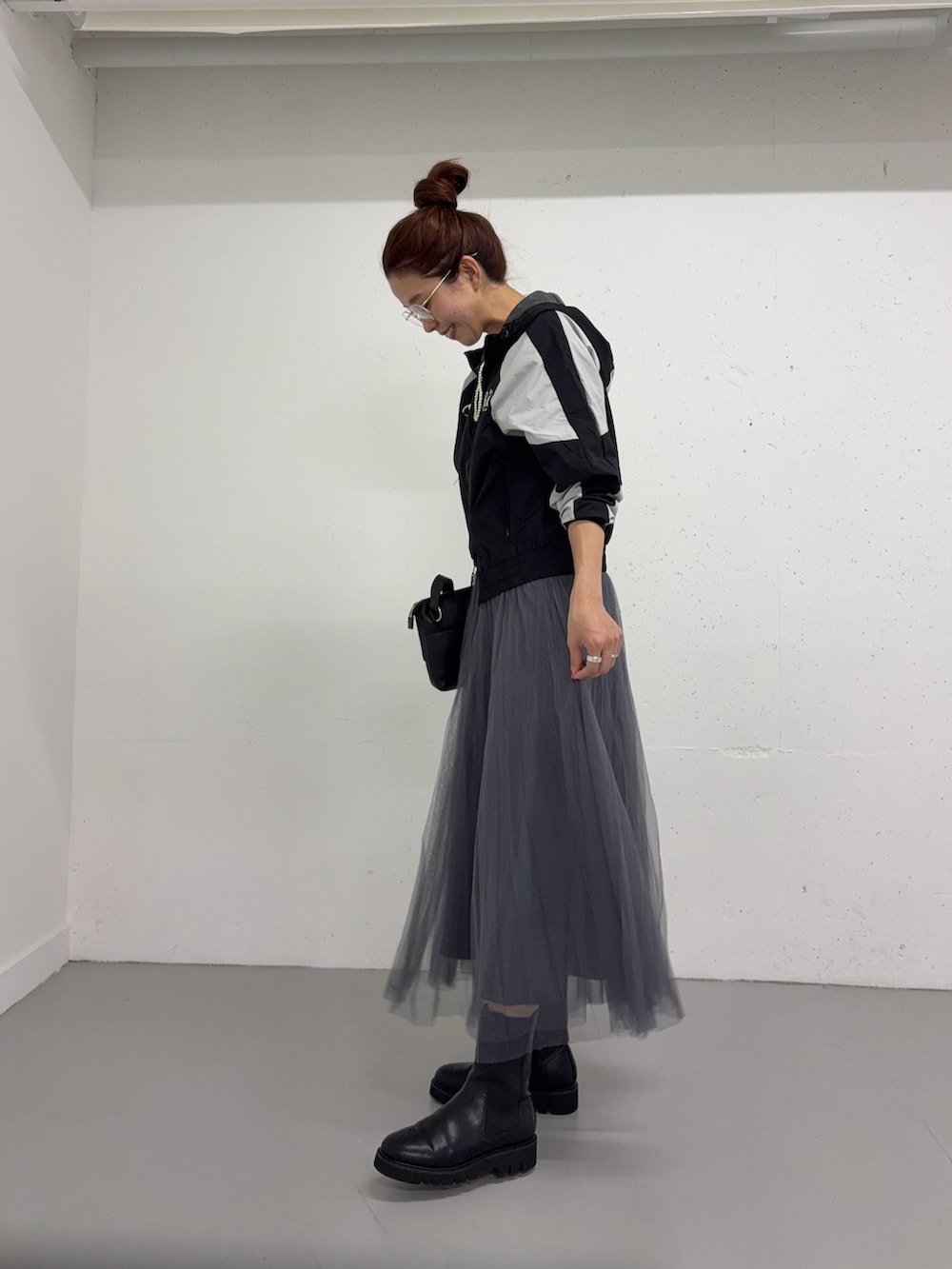 グレー系のスカート、ブラック系のナイロンジャケット、ブラック系のブーツを着用したレディースの夏コーディネートの2枚目の写真