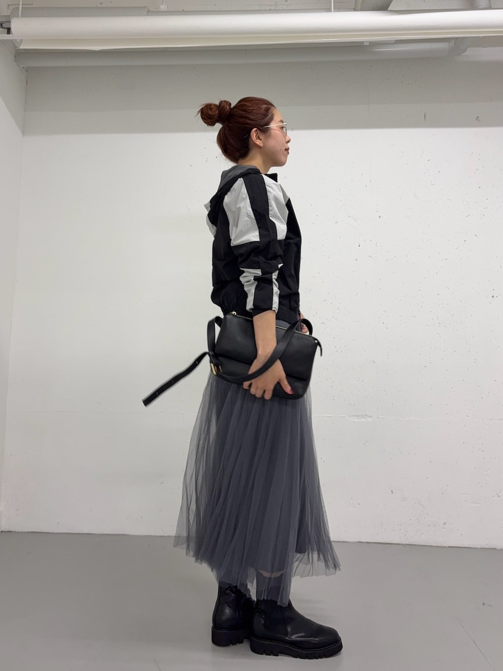 グレー系のスカート、ブラック系のナイロンジャケット、ブラック系のブーツを着用したレディースの夏コーディネートの4枚目の写真