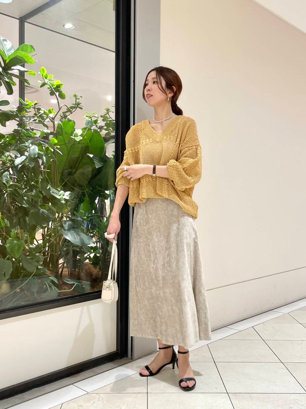 ホワイト系のショルダーバッグ、ベージュ系のスカート、イエロー系のニット/セーターを着用したレディースの冬コーディネートの2枚目の写真