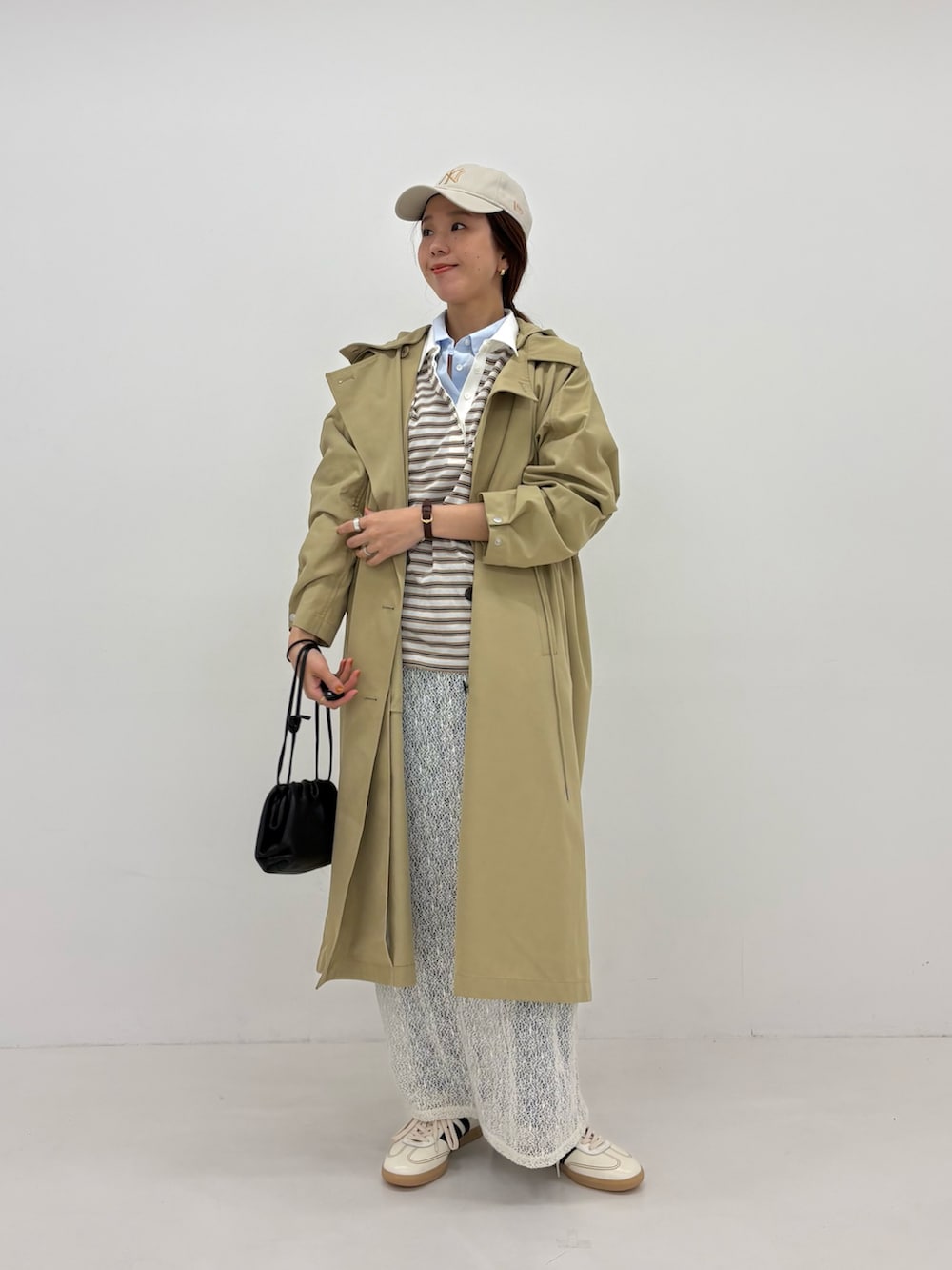 ホワイト系のスカート、ベージュ系のトレンチコート、ホワイト系のスニーカーを着用したレディースの春コーディネートの2枚目の写真