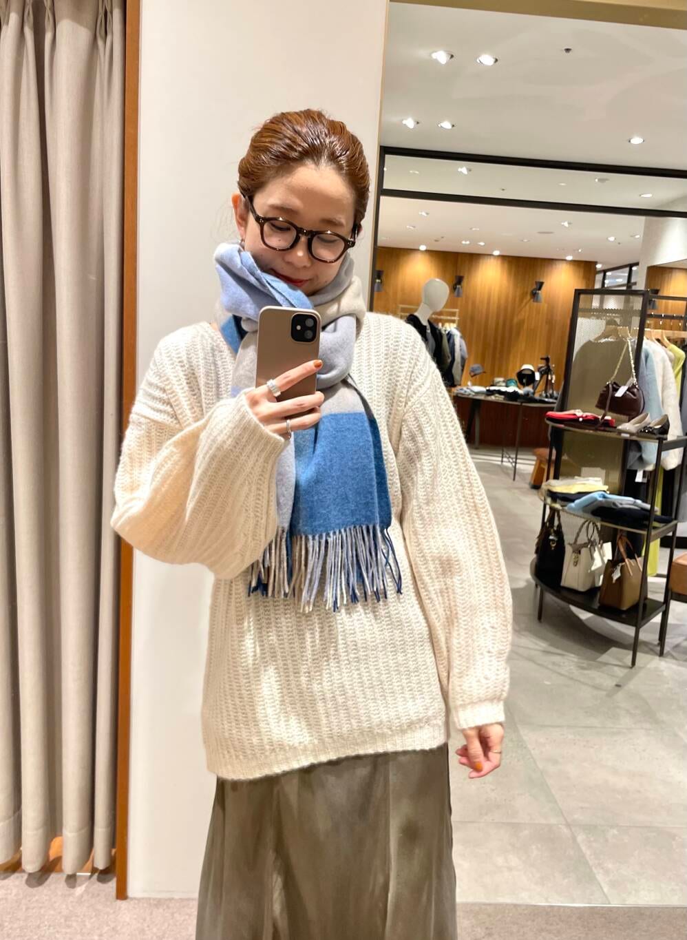 グリーン系のスカート、ホワイト系のニット/セーター、ブルー系のマフラーを着用したレディースの冬コーディネートの2枚目の写真