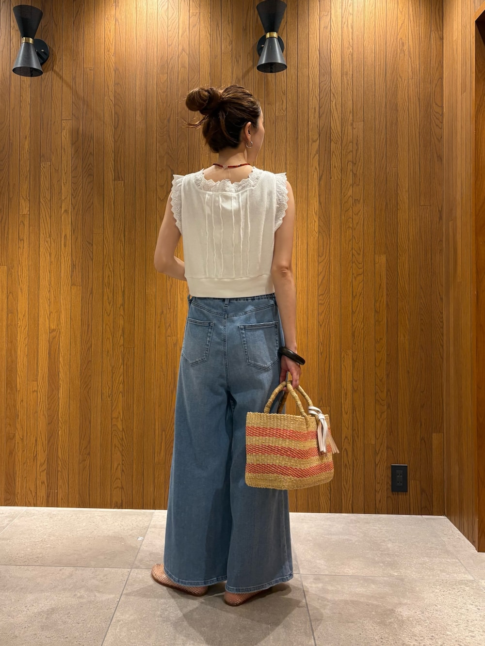 ブルー系のデニムパンツ、ホワイト系のベスト、ベージュ系のかごバッグを着用したレディースの夏コーディネートの3枚目の写真