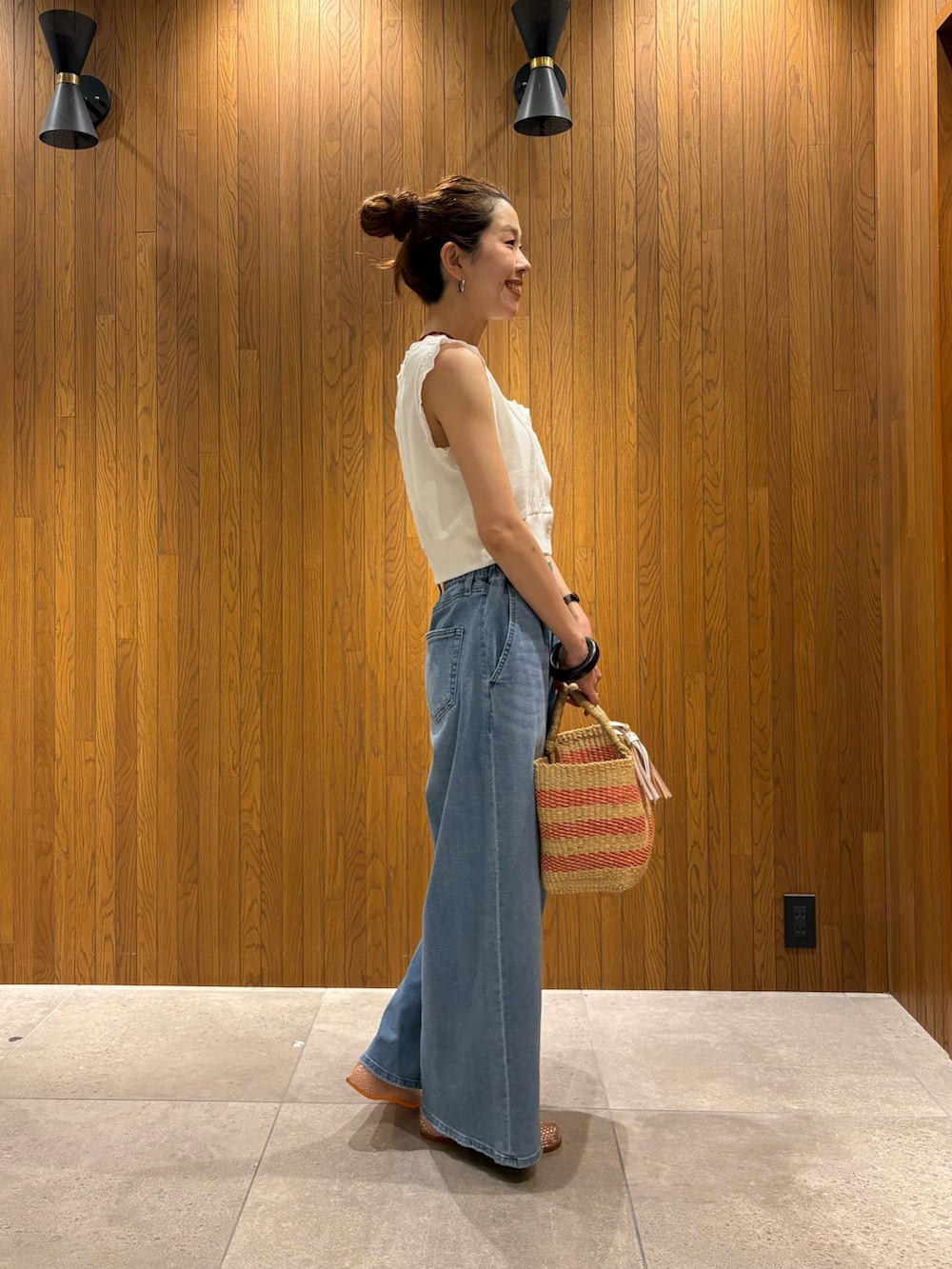 ブルー系のデニムパンツ、ホワイト系のベスト、ベージュ系のかごバッグを着用したレディースの夏コーディネートの4枚目の写真