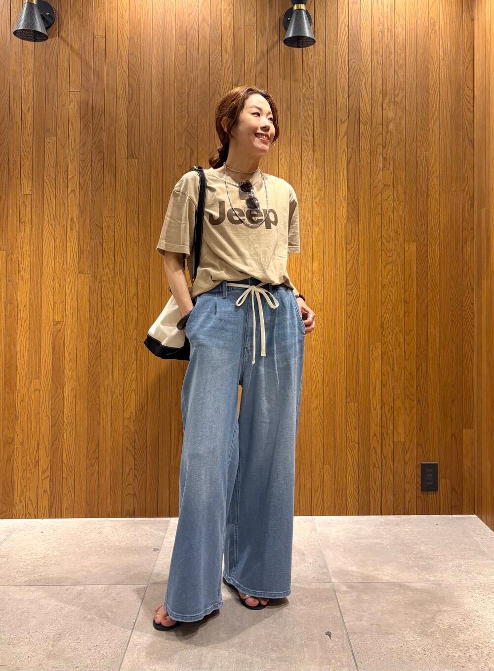 ブルー系のデニムパンツ、ブラック系のサンダル、ベージュ系のTシャツ/カットソーを着用したレディースの夏コーディネートの4枚目の写真