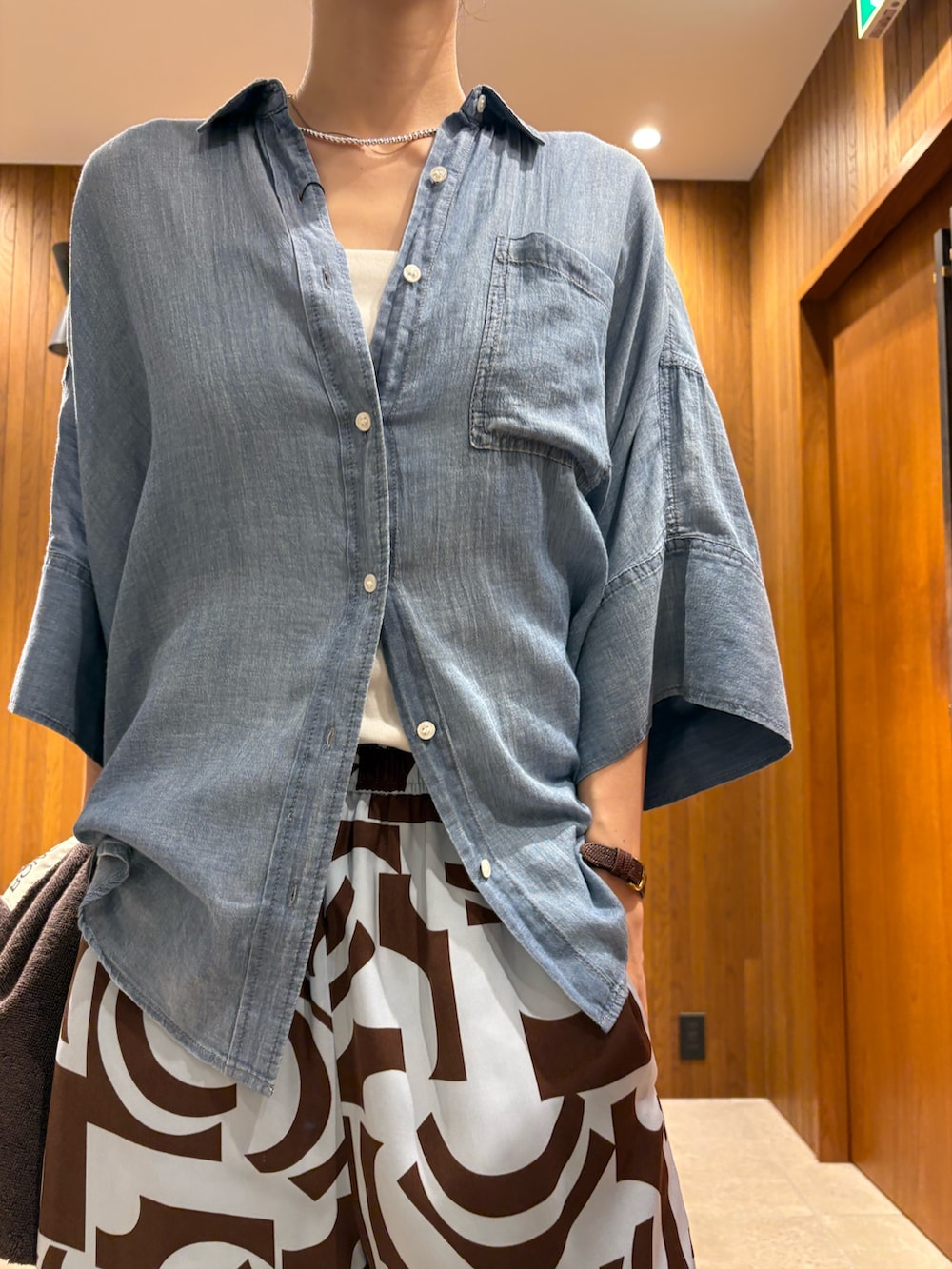 ブルー系のシャツ/ブラウス、ブラウン系のトートバッグ、ブラック系のサンダルを着用したレディースの夏コーディネートの6枚目の写真