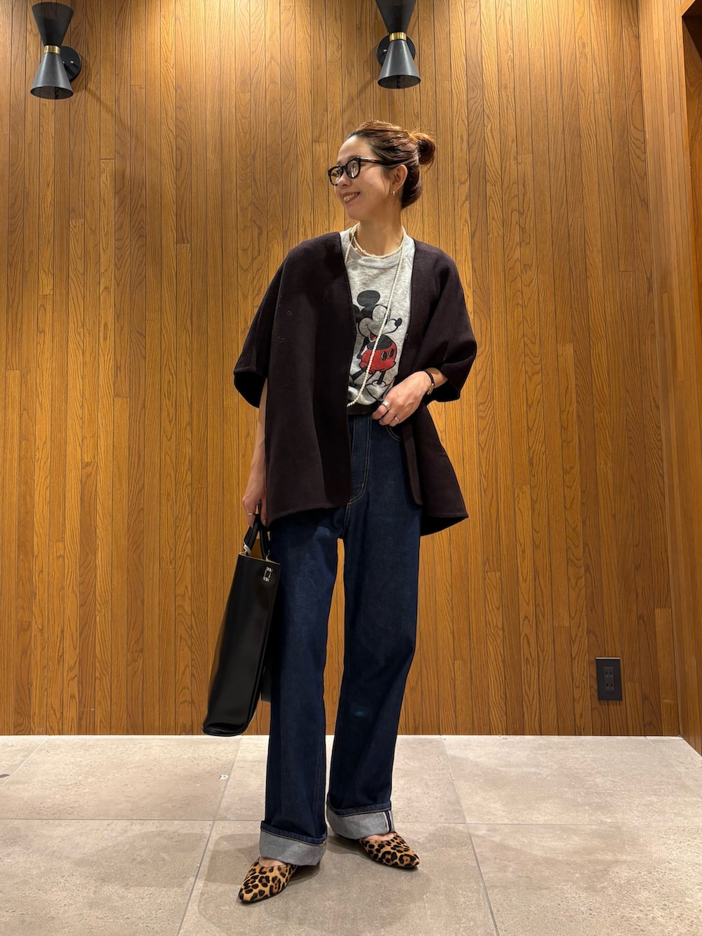 レッド系のポンチョ、ブルー系のデニムパンツ、ブラック系のトートバッグを着用したレディースの秋コーディネートの7枚目の写真