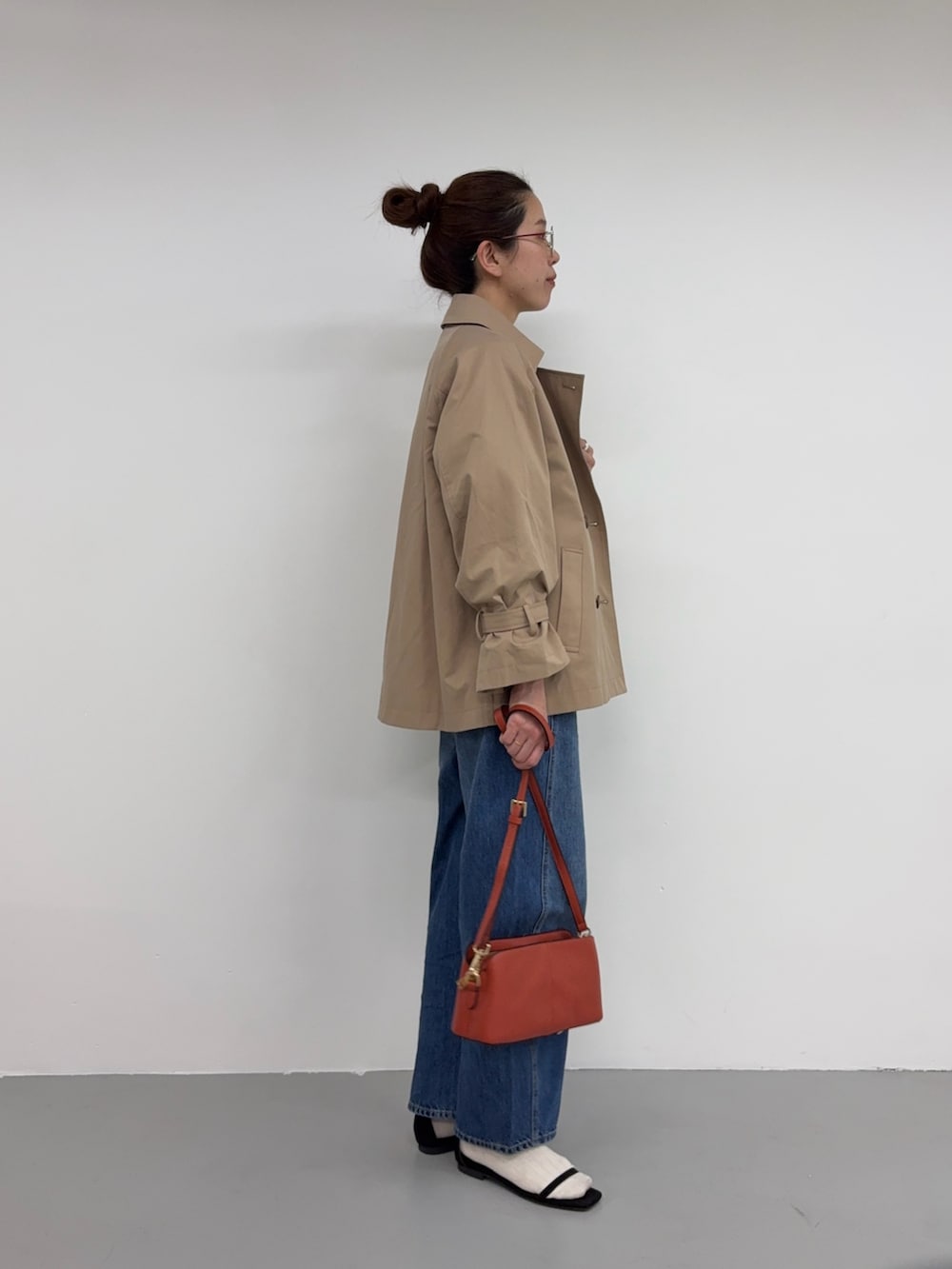 ベージュ系のトレンチコート、ブルー系のデニムパンツ、オレンジ系のショルダーバッグを着用したレディースの冬コーディネートの2枚目の写真