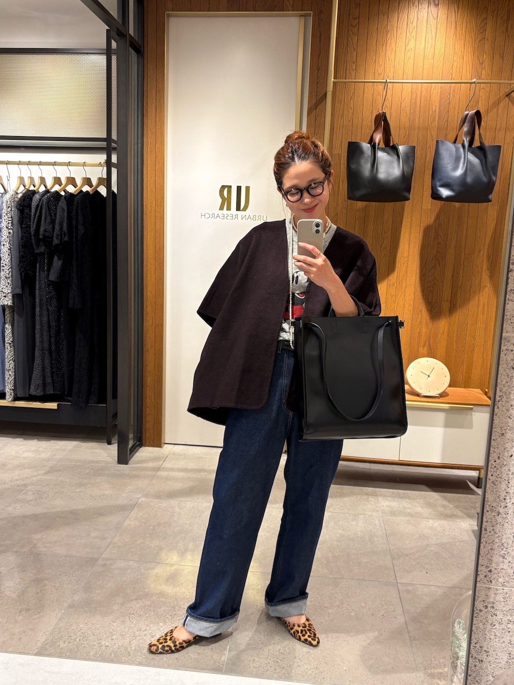 レッド系のポンチョ、ブルー系のデニムパンツ、ブラック系のトートバッグを着用したレディースの秋コーディネートの9枚目の写真