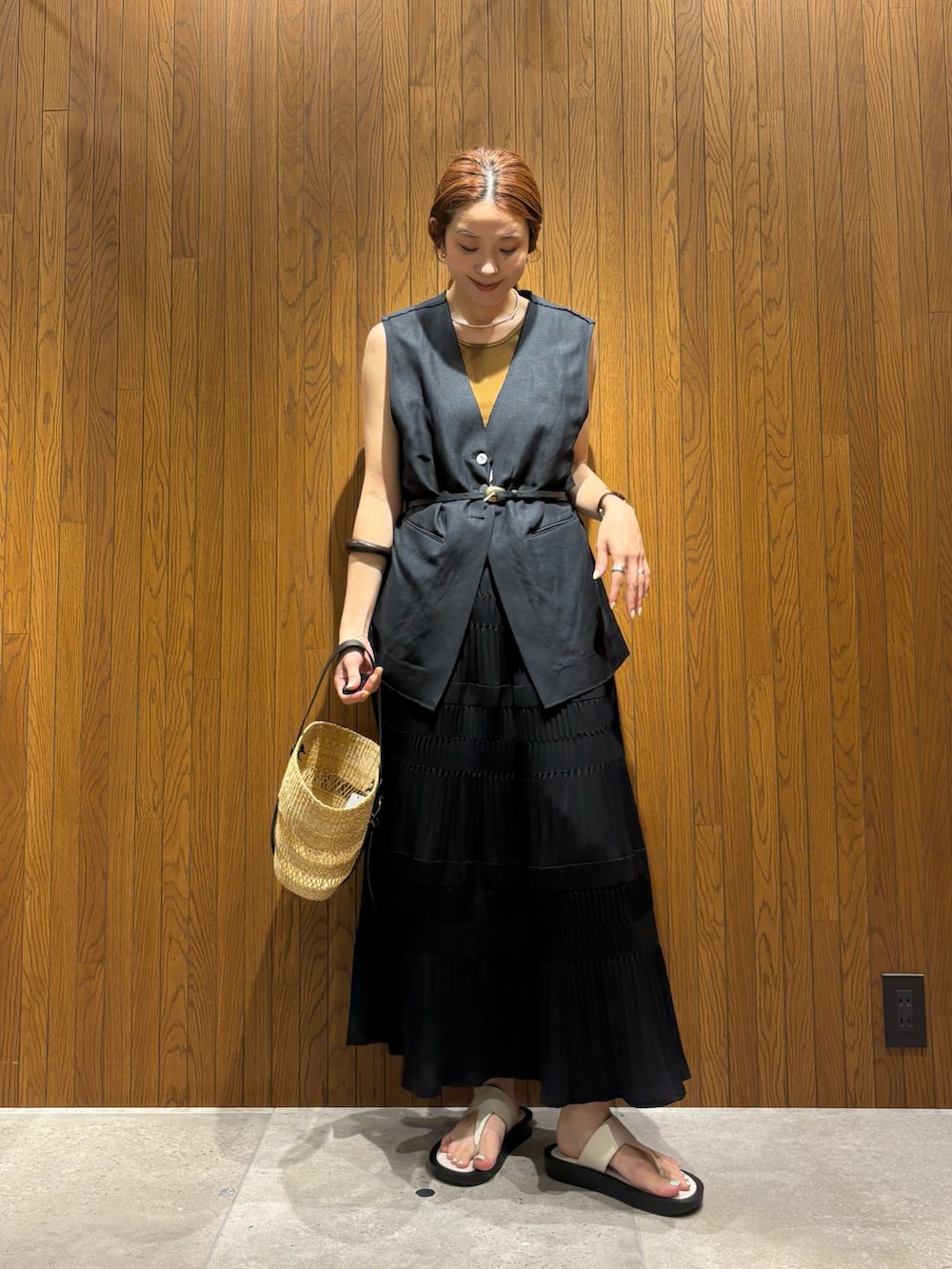 ブラック系のスカート、ベージュ系のかごバッグ、ブラック系のダウンベストを着用したレディースの夏コーディネートの5枚目の写真