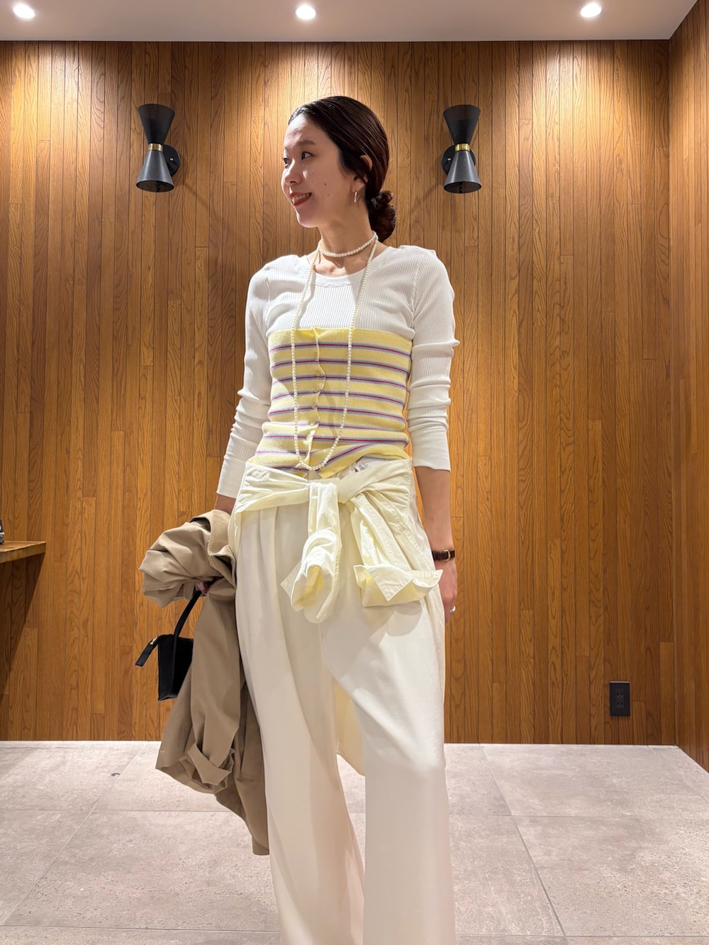 ベージュ系のトレンチコート、イエロー系のニット/セーター、ホワイト系のその他パンツを着用したレディースの春コーディネートの9枚目の写真