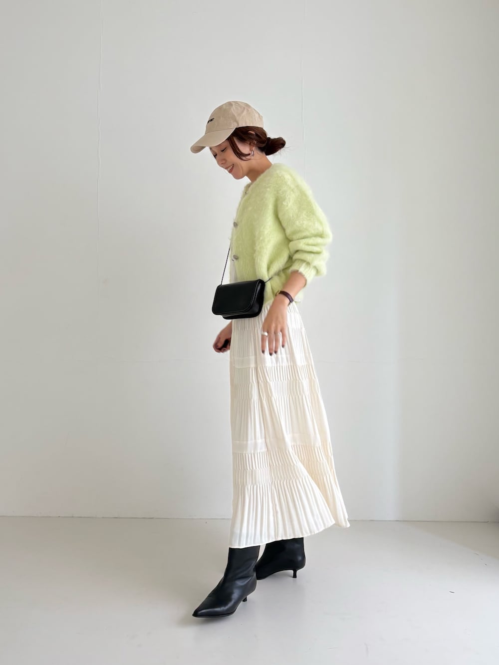 ホワイト系のスカート、グリーン系のカーディガン/ボレロ、ブラック系のブーツを着用したレディースの秋コーディネートの2枚目の写真