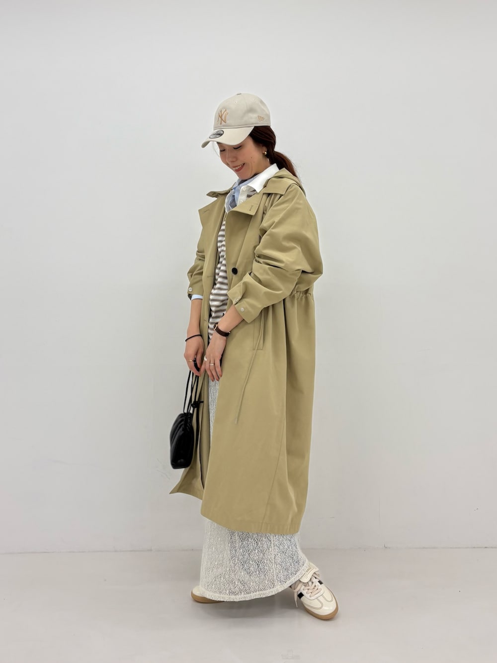 ホワイト系のスカート、ベージュ系のトレンチコート、ホワイト系のスニーカーを着用したレディースの春コーディネートの3枚目の写真
