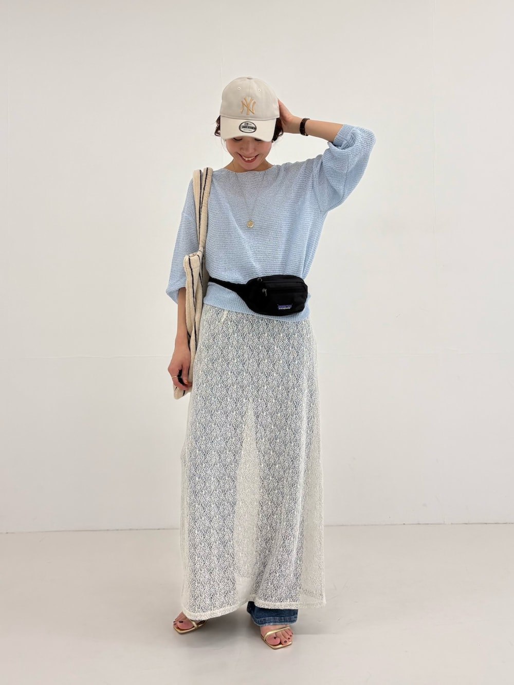 ブルー系のニット/セーター、ホワイト系のスカート、ブラック系のボディバッグ/ウエストポーチを着用したレディースの春コーディネートの2枚目の写真