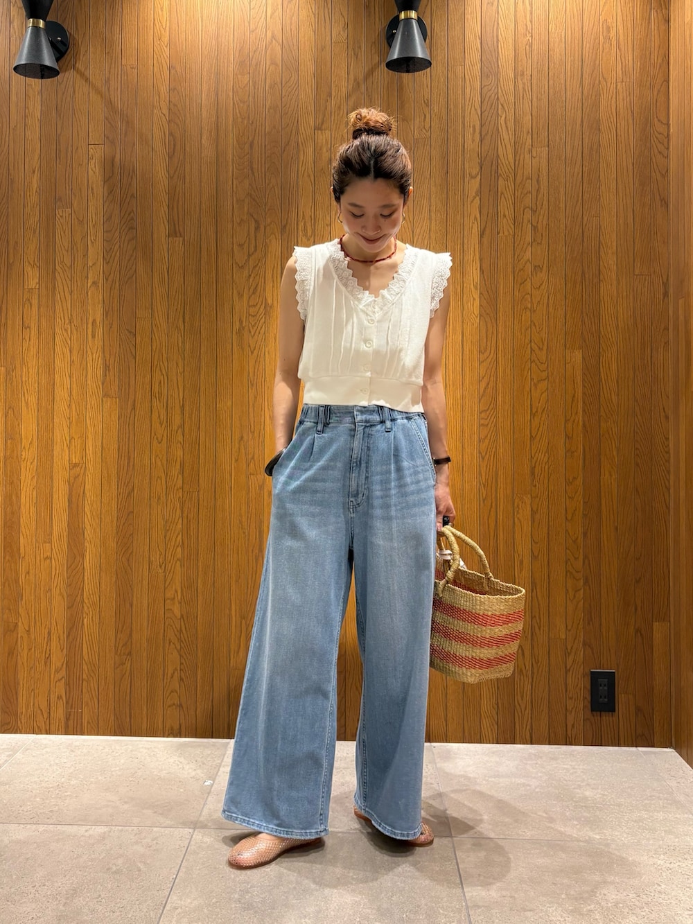 ブルー系のデニムパンツ、ホワイト系のベスト、ベージュ系のかごバッグを着用したレディースの夏コーディネートの5枚目の写真