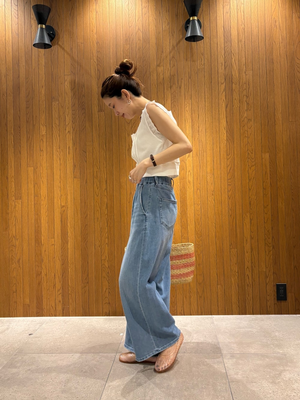 ブルー系のデニムパンツ、ホワイト系のベスト、ベージュ系のかごバッグを着用したレディースの夏コーディネートの2枚目の写真
